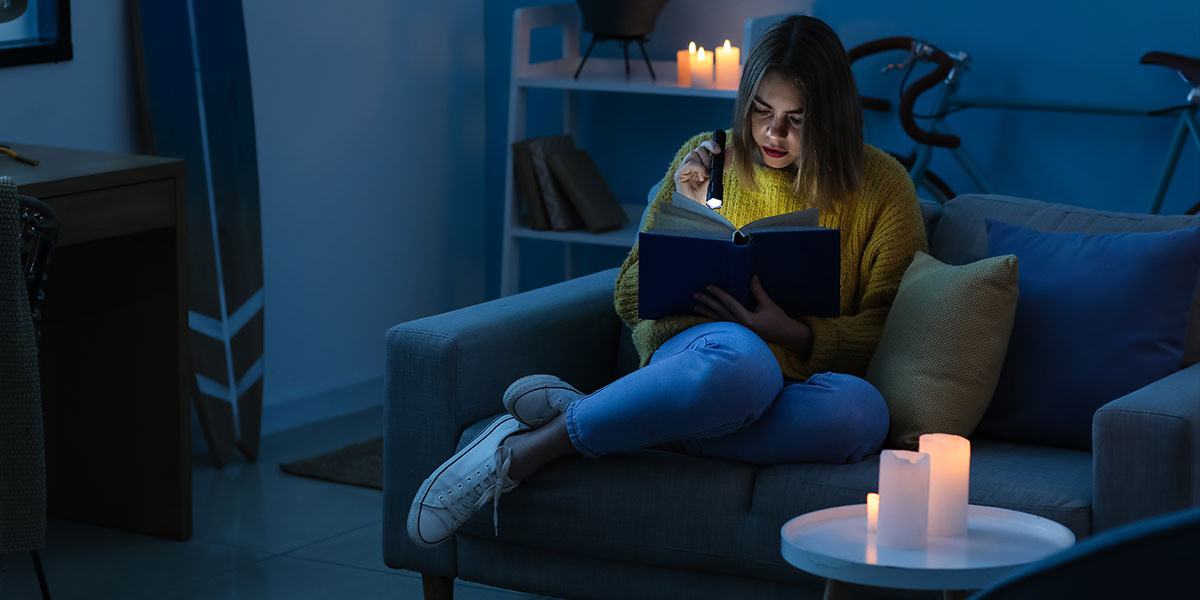 Kobieta czytająca książkę przy świetle latarki i świec