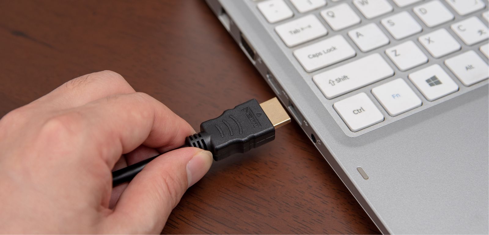 osoba podpina wtyczkę HDMI do laptopa