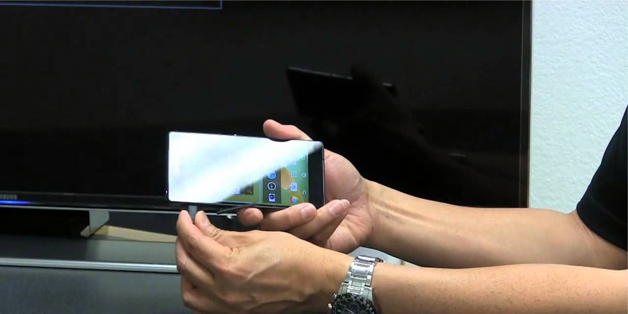 mężczyzna podłącza kabel USB to smartfona na tle telewizora LCD